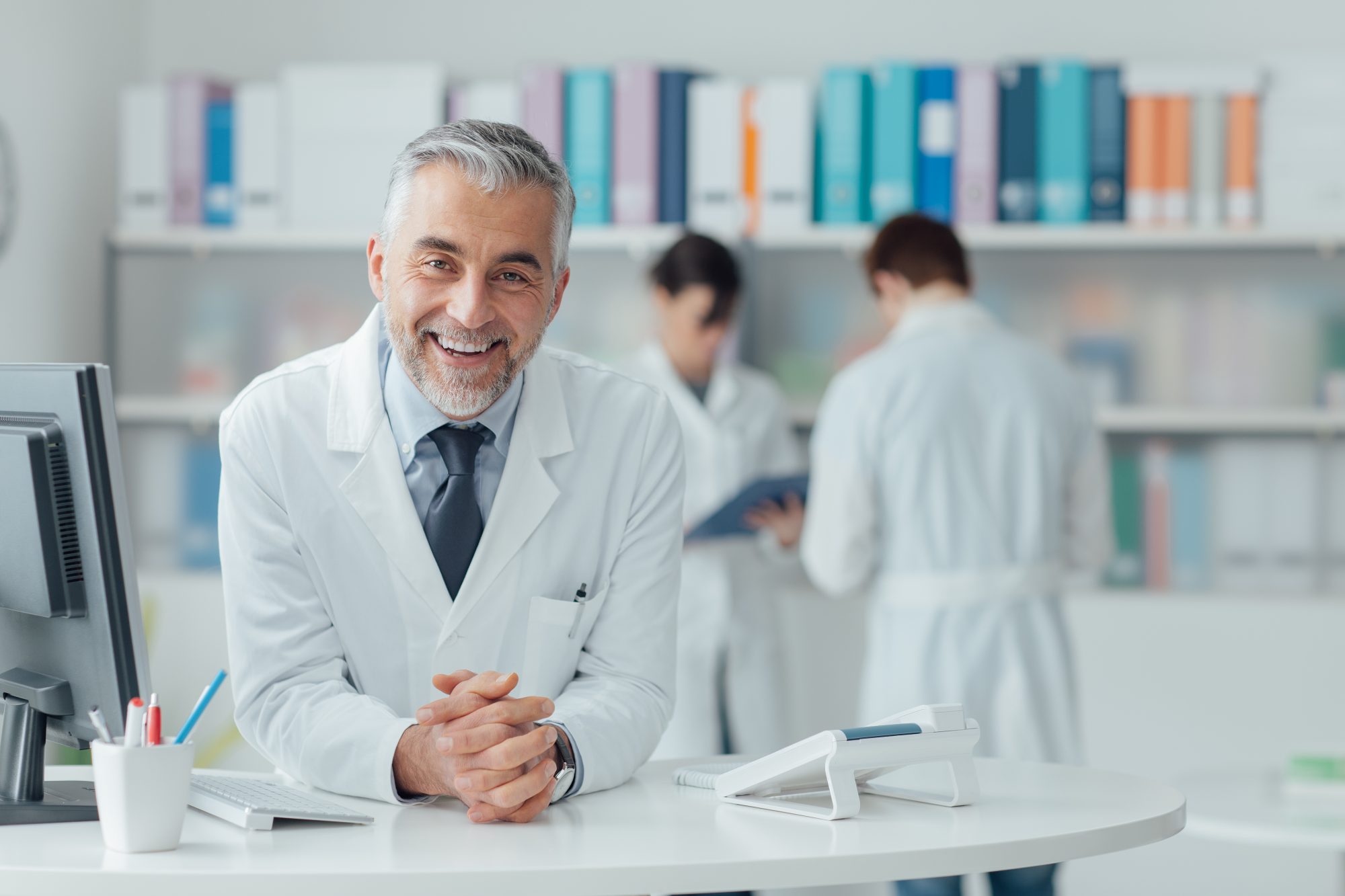 Physician in white lab coat behind front desk ready to consult patients